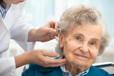 Doctor inserting hearing aid in seniors ear